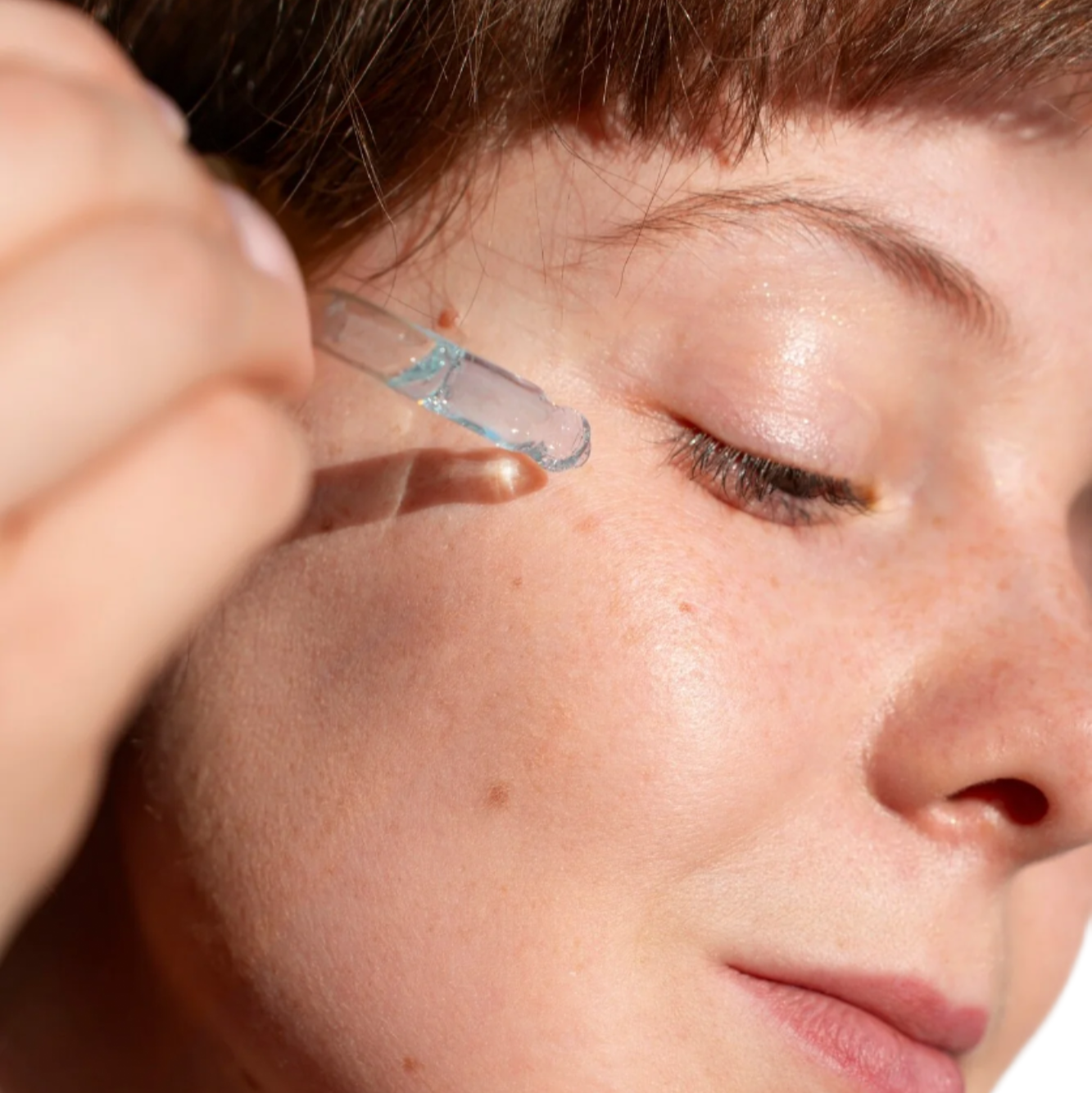 White woman red hair with dropper applying best face serum for acne and large pores. Dermal Essentials Clinical Skincare.