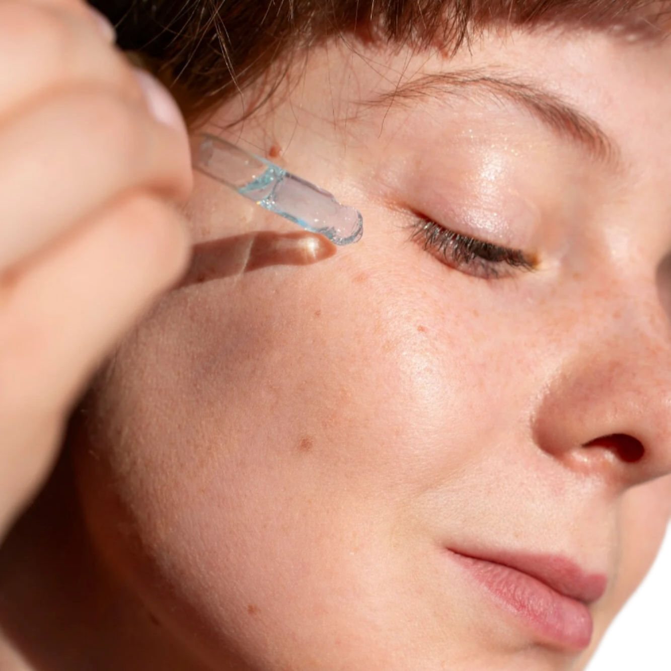 White woman red hair with dropper applying best face serum for acne and large pores. Dermal Essentials Clinical Skincare.