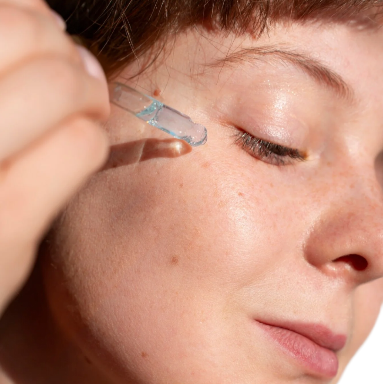 White woman red hair with dropper applying best face serum for acne and large pores. Dermal Essentials Clinical Skincare.