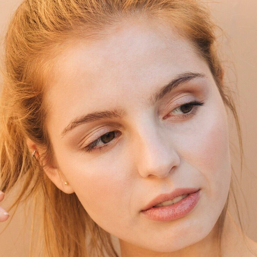 white woman red hair brown eyebrows gold stud earrings dermal essentials medical grade skincare