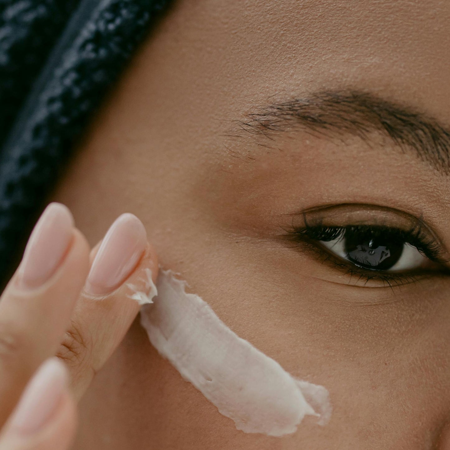 black woman black hair brown eye applying white eye cream dermal essentials medical grade skincare