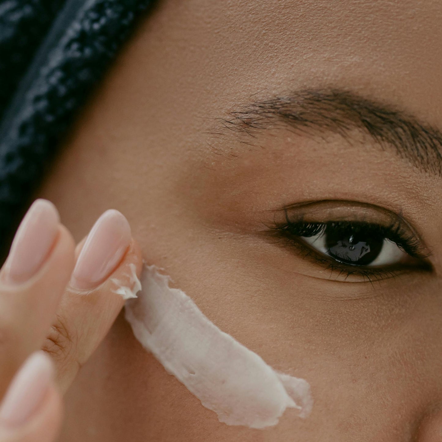 black woman black hair brown eye applying white eye cream dermal essentials medical grade skincare