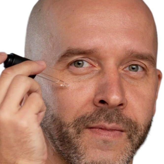 White bald man with beard using black dropper to apply best skin plumping serum. Dermal Essentials Medical Grade Skincare.