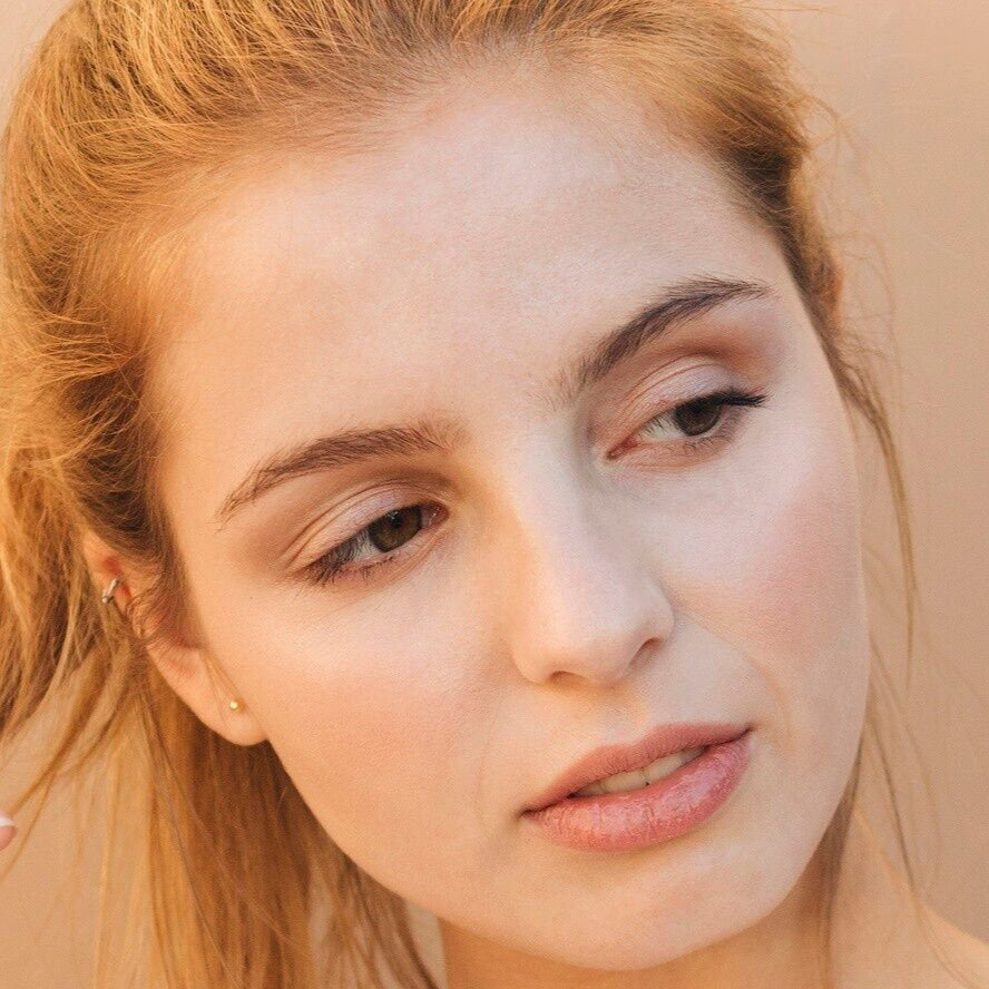 white woman red hair brown eyebrows gold stud earrings dermal essentials medical grade skincare