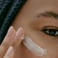 black woman black hair brown eye applying white eye cream dermal essentials medical grade skincare