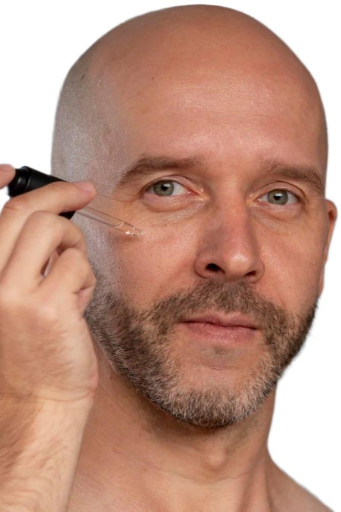 White bald man with beard using black dropper to apply best skin plumping serum. Dermal Essentials Medical Grade Skincare.