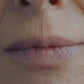 A close-up split comparison photo of a person's lower face, focusing on the lips and upper lip area. A subtle vertical line down the center divides the image into two sides. The left side displays natural fine vertical lines and wrinkles on the upper lip area, while the right side shows a smooth, wrinkle-free upper lip, demonstrating a before-and-after treatment effect.