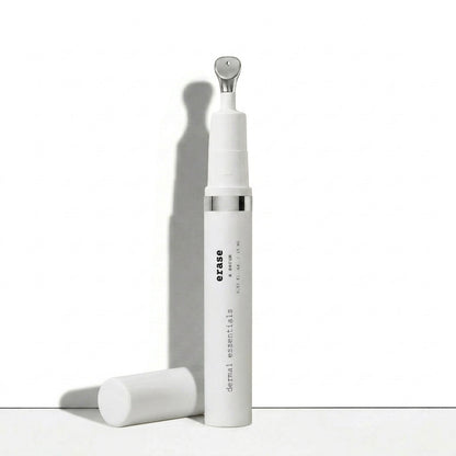 A white cylindrical skincare bottle labeled 'erase dermal essentials' with a silver metallic neck detail, shown standing upright with its cap placed beside it on a clean white surface.