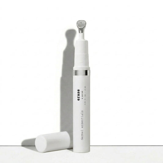 A white cylindrical skincare bottle labeled 'erase dermal essentials' with a silver metallic neck detail, shown standing upright with its cap placed beside it on a clean white surface.